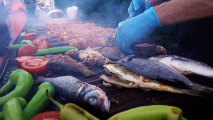 Barbecue party in the open air. The chief is frying meat, vegetables and fish on the grill.