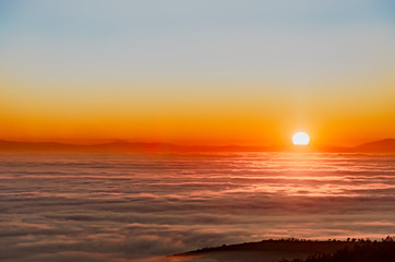 Beautiful misty sunset over mountain summit covvere3d with fog, aerial view, view on clouds from above, bright sun