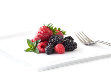 A plate of berries and a fork on a white background