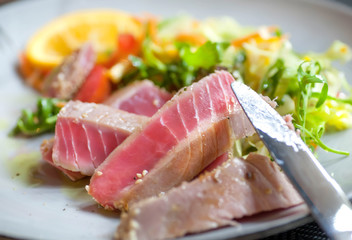 Fish tuna meat dish on plate with orange and vegetables. Food of modern mediterranian restaurant.