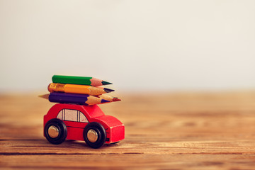 Back to school concept. Miniature Red Car Carrying a colorful pencils on wooden table.