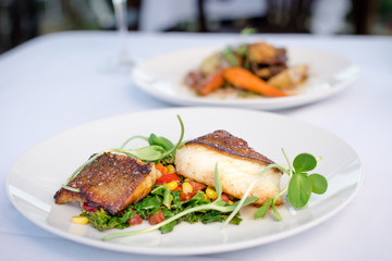 Pan roasted sable fish with spring vegetables on a white plate in a restaurant.