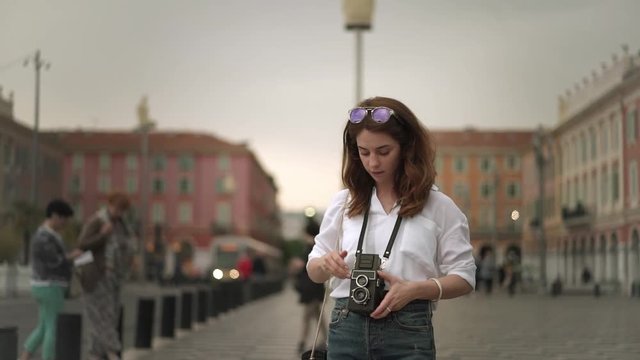 Beautiful woman photographer in white shirt with long dark hair making shots of Nice, France with old school camera. A tram. Cloudy spring day. Handheld slow motion medium shot