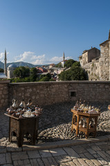Bosnia Erzegovina: un tavolino con set di rame di tè e caffè in vendita e vista sullo skyline di Mostar con la moschea Koshi Mehmed Pasha sullo sfondo
