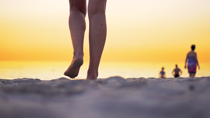 Bare legs feet of young Latin American girl walking by ocean beach at sunset
