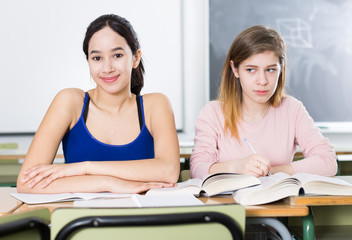 Portrait schoolgirl who is envying her successful girlfriend at the desk