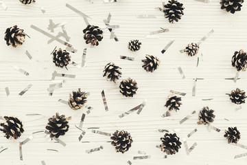 christmas flat lay. modern christmas layout with golden pine cones and silver confetti  on white wood, top view. holiday mockup greeting card. stylish winter flatlay. pinecone pattern