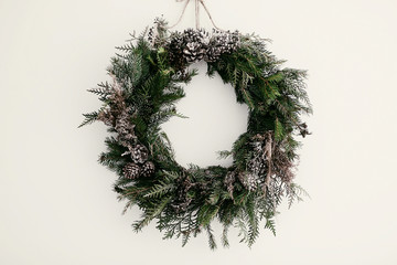 modern Christmas wreath. stylish rustic christmas wreath with pine cones,fir branches,snow, hanging on white wall. space for text. handmade decor for winter holidays © sonyachny