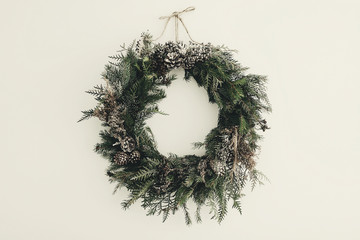 modern Christmas wreath. stylish rustic christmas wreath with pine cones,fir branches,snow, hanging on white wall. space for text. handmade decor for winter holidays