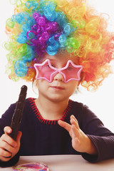 Humorous portrait of cute little girl with colorful curly hair using flat Iron . Hair beauty, hair care concept.