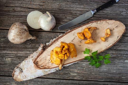 Forest mushrooms chanterelle on wooden birch board with white onions. Ingredients for mushroom sauce cooking. Top view, close-up on wooden background