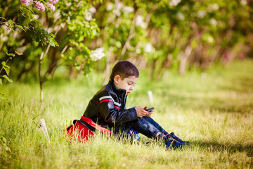 Naklejka na ściany i meble Little boy sitting on the grass in the spring park