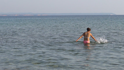 Lonely young woman plays alone in sea shallow water splashing with her hands