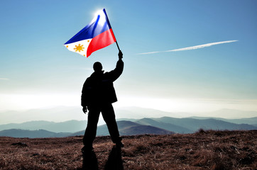Successful silhouette man winner waving Philippines flag on top of the mountain peak