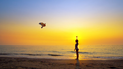 Fototapeta na wymiar Boy launch a kite running on beach at sunset, cinematic steadicam shot