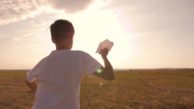 A boy in the field at sunset runs and throws a paper plane. The concept of a happy child