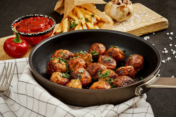 delicious meat balls in a pan and golden crispy fries on a black old table