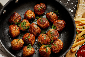 delicious meat balls in a pan and golden crispy fries on a black old table