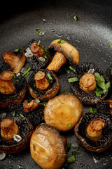 delicious fried mushrooms on a hot pan on an old wooden black table