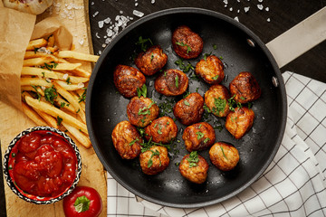 delicious meat balls in a pan and golden crispy fries on a black old table