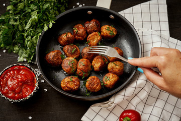 hand with a fork over a pan with delicious meatballs with parsley