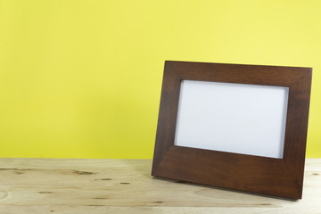 Photo frame on wooden table over yellow background,copy space.