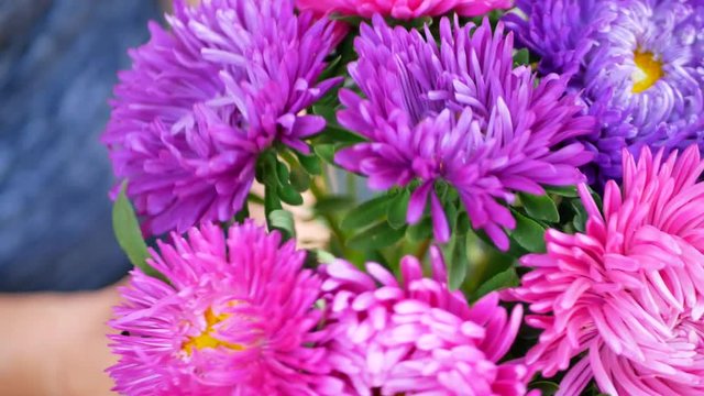 Woman florist's hands making bouquet with pink, purple or violet michaelmas daisy or aster flower on table for flower shop outdoor