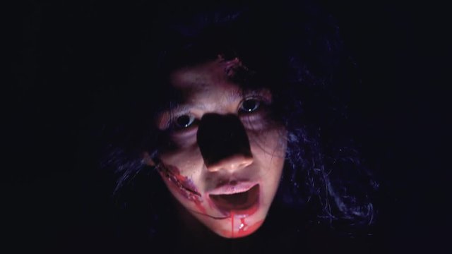 Scary zombie woman face with bloody mouth staring at camera in dark. Shot in 4k resolution