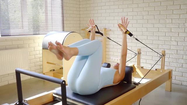 woman is training on a moving platform of equipment for pilates exercises in a fitness room