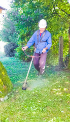 A man in overalls mows the grass with a lawn mower