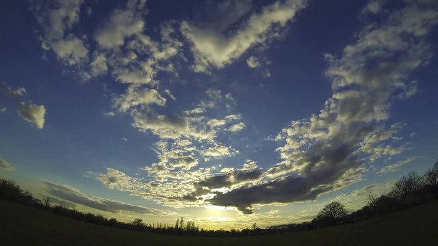 Time Lapse video of a sunny sunset with clouds in a park in West London, Uk. Big airplane traffic on the sky for the proximity of the International Airport of Heathrow. Ultra wide angle lens view.