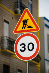 Round signage of with speed limit and triangle sign showing road repair works in sunlight