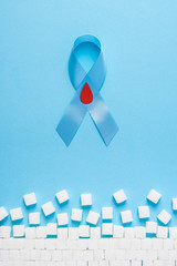 blue ribbon awareness with red blood drop and ruined wall made of sugar cubes on a blue background,...