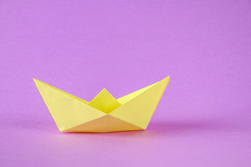 Yellow paper boat from origami with an autumn leaf on a purple background.