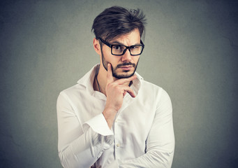 Doubtful young man in glasses looking at camera