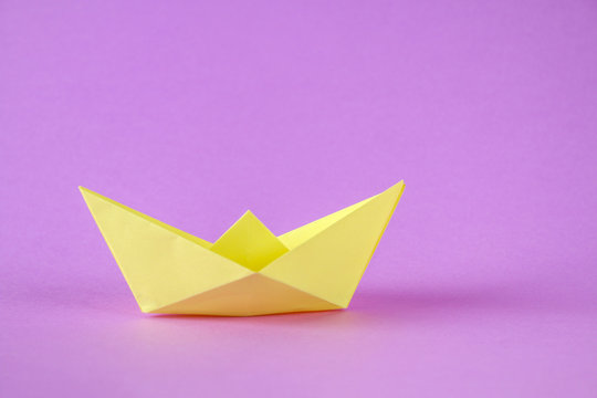 Yellow Paper Boat From Origami With An Autumn Leaf On A Purple Background.