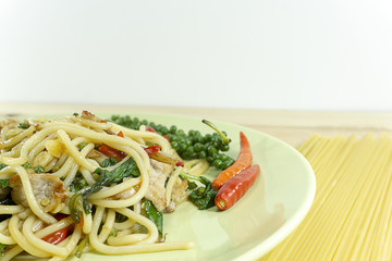 Spaghetti fried with spicy pork in a white dish on wood table, props decoration with pepper red, tomatoes ,Copy space, Close up.
