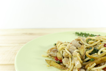 Spaghetti fried with spicy pork yellow line in a green dish on a wooden background, props decoration with fresh pepper red, tomatoes,Copy space Close up.