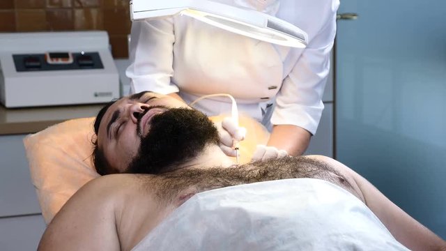 Brutal darkhaired man in healthcare clinic. Dermatologist makes electrocoagulation. 4k