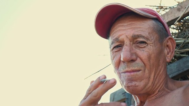 Portrait of a smoking hard worker against the background of a rural scene. A farmer in a cap smokes a cigarette