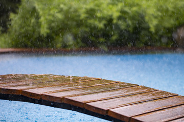 drops of rain fall on a wooden terrace and a bridge near the pool close up