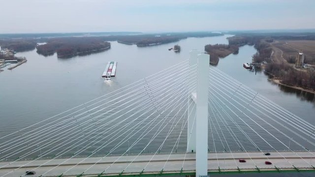 Aerial of a coal barge pushed by tugboat moving up the Mississippi River near Burlington Iowa with suspension bridge foreground.