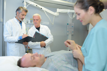 Nurse holding hand of patient while doctors confer