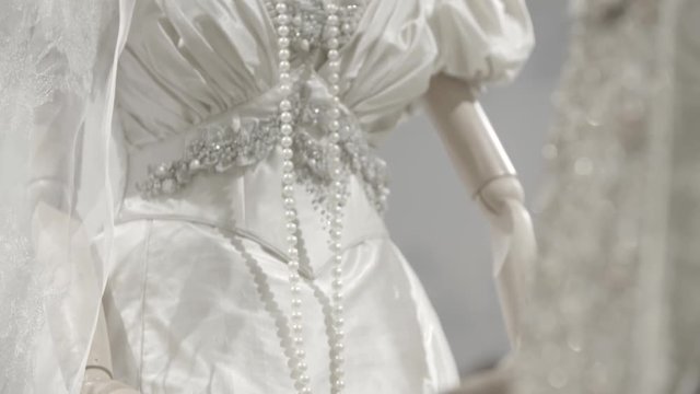 A white lacy dress on a female mannequin. Dettail of a wedding gown with necklace made of pearls. Fashion concept.