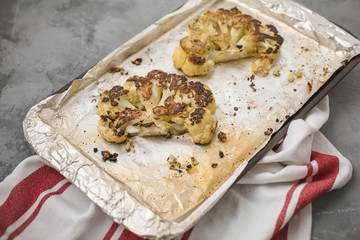 Cauliflower Steaks on a Rimmed Baking Sheet; Gray Background