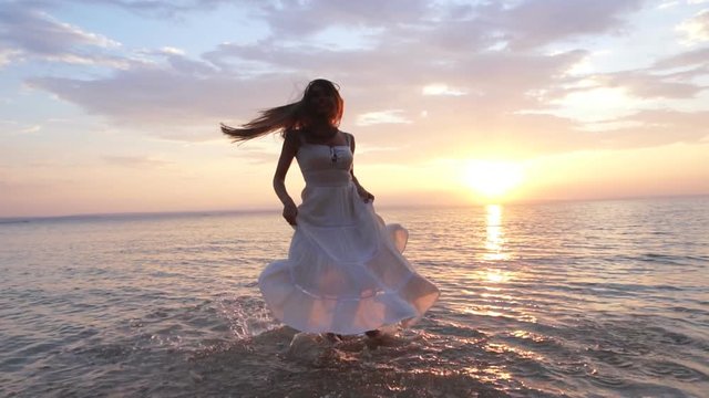 young woman in sundress spinning in the water on the shore