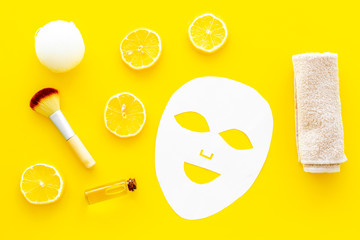 Face spa products. Facial mask, cream, oil near lemon slices and towel on yellow background top view