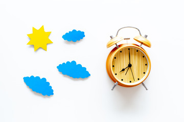 Time of day. Morning. Awakening and sunrise. Sun and clouds cutout near alarm clock on white background top view