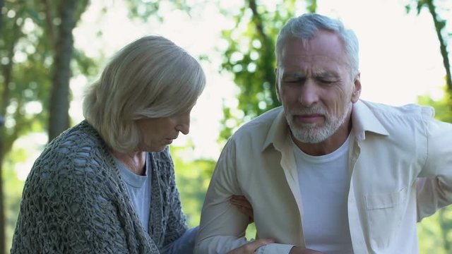 Mature man feeling sharp back pain while walking in park caring wife helping him