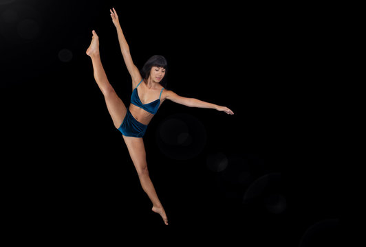 Ballet female dancer performing a leap on stage with a black backdrop
